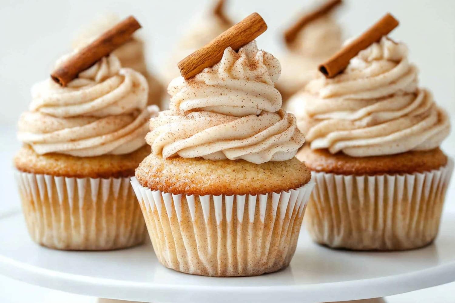 Snickerdoodle cupcakes topped with creamy frosting sitting on a cake tray.