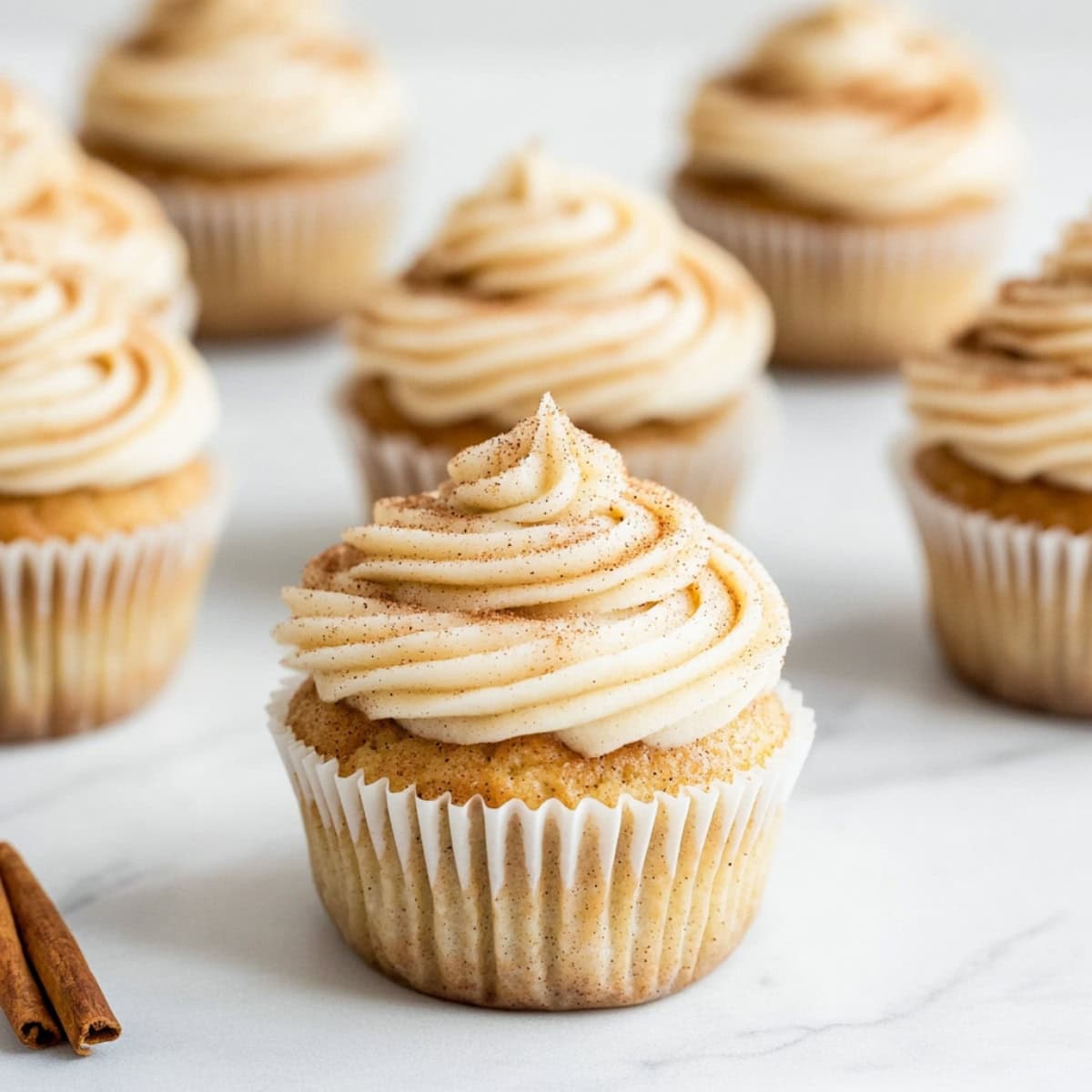 Snickerdoodle cupcakes with cinnamon frosting sitting on a white marble table.