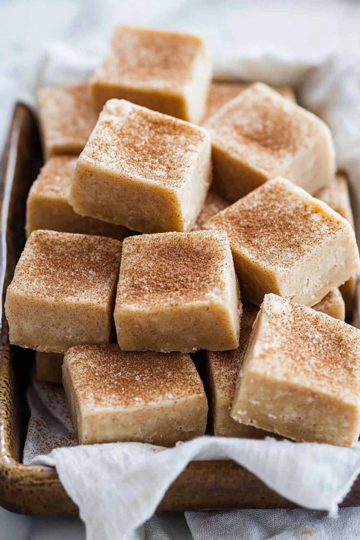 Square servings of snickerdoodle fudge in a baking pan lined with parchment paper