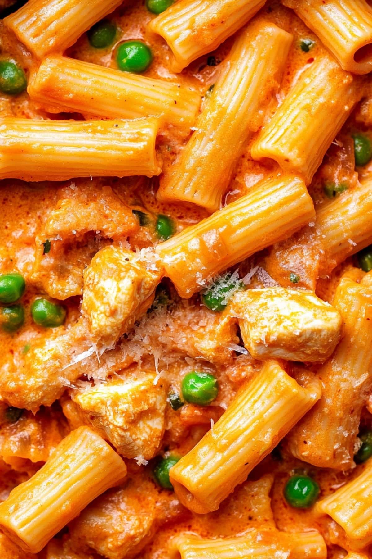 A close-up of spicy chicken rigatoni with green peas and shredded parmesan.