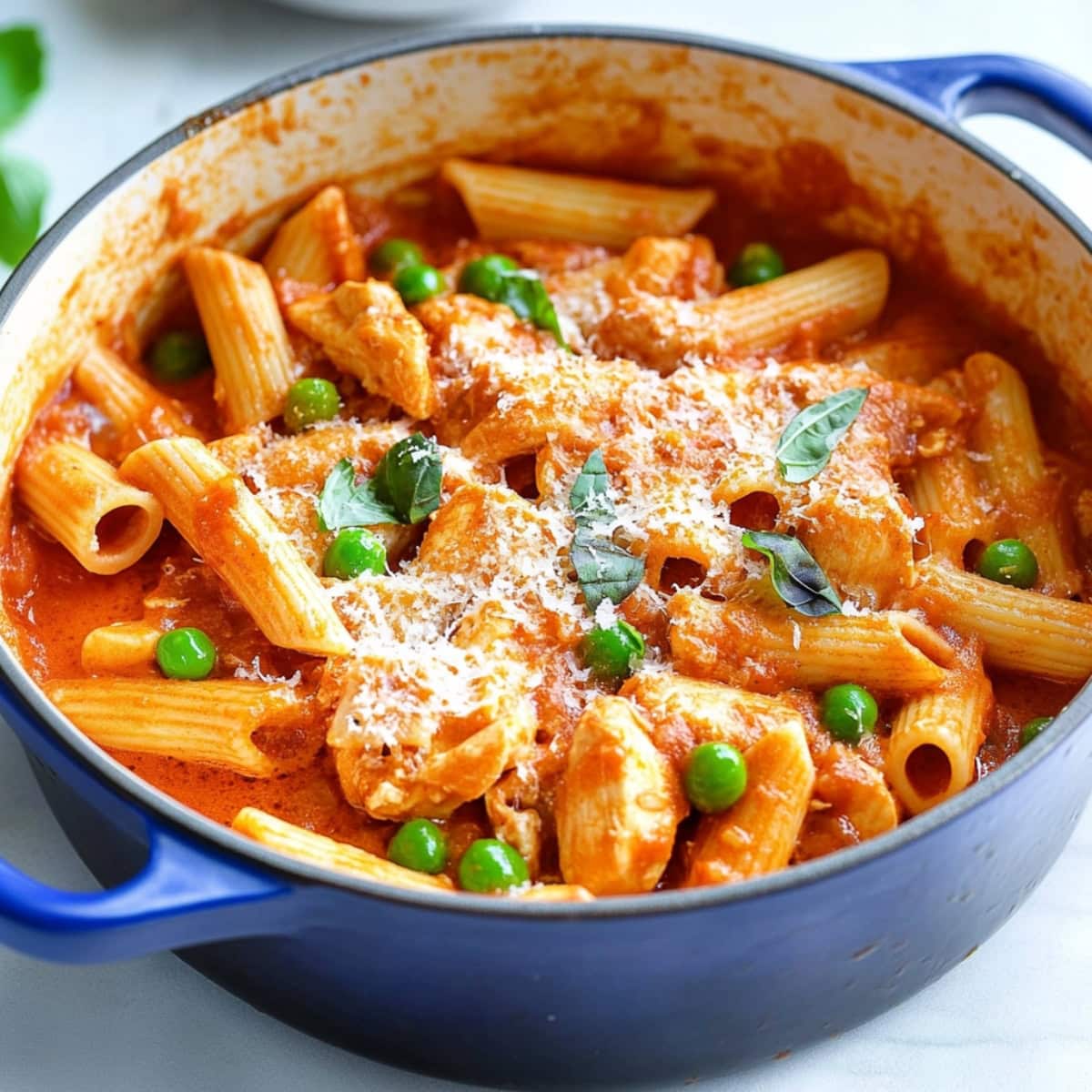 A large pot of spicy chicken rigatoni with green pease, shredded parmesan, garnished with chopped parmesan.