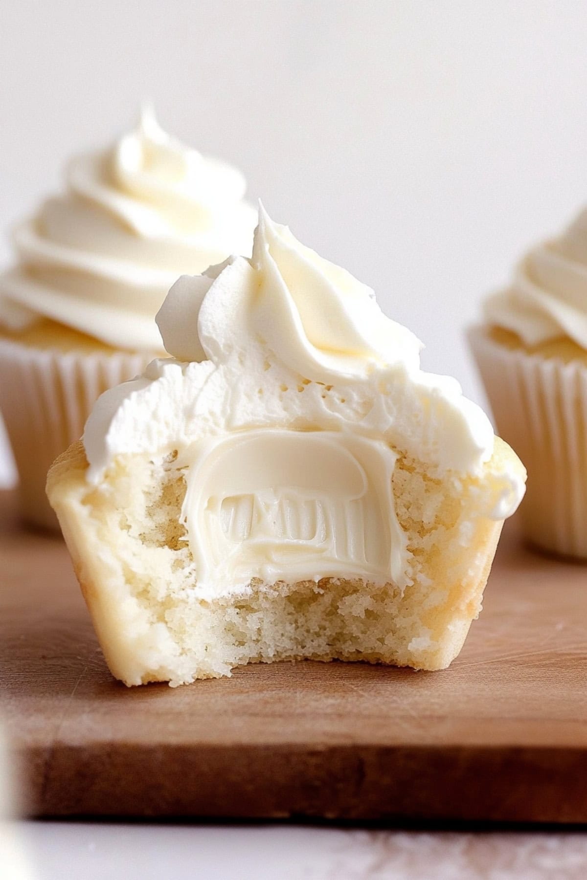 A white chocolate cupcake with frosting cut in half to show the creamy ganache filling. 