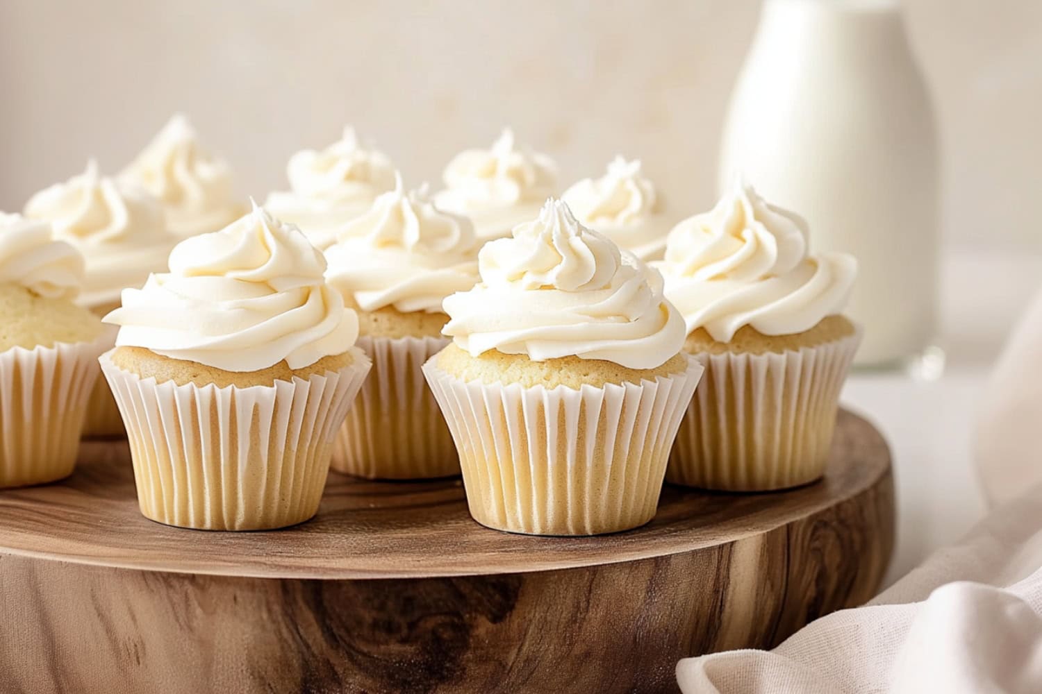 White chocolate cupcakes with creamy frosting in a wooden board, a glass of milk in the background.