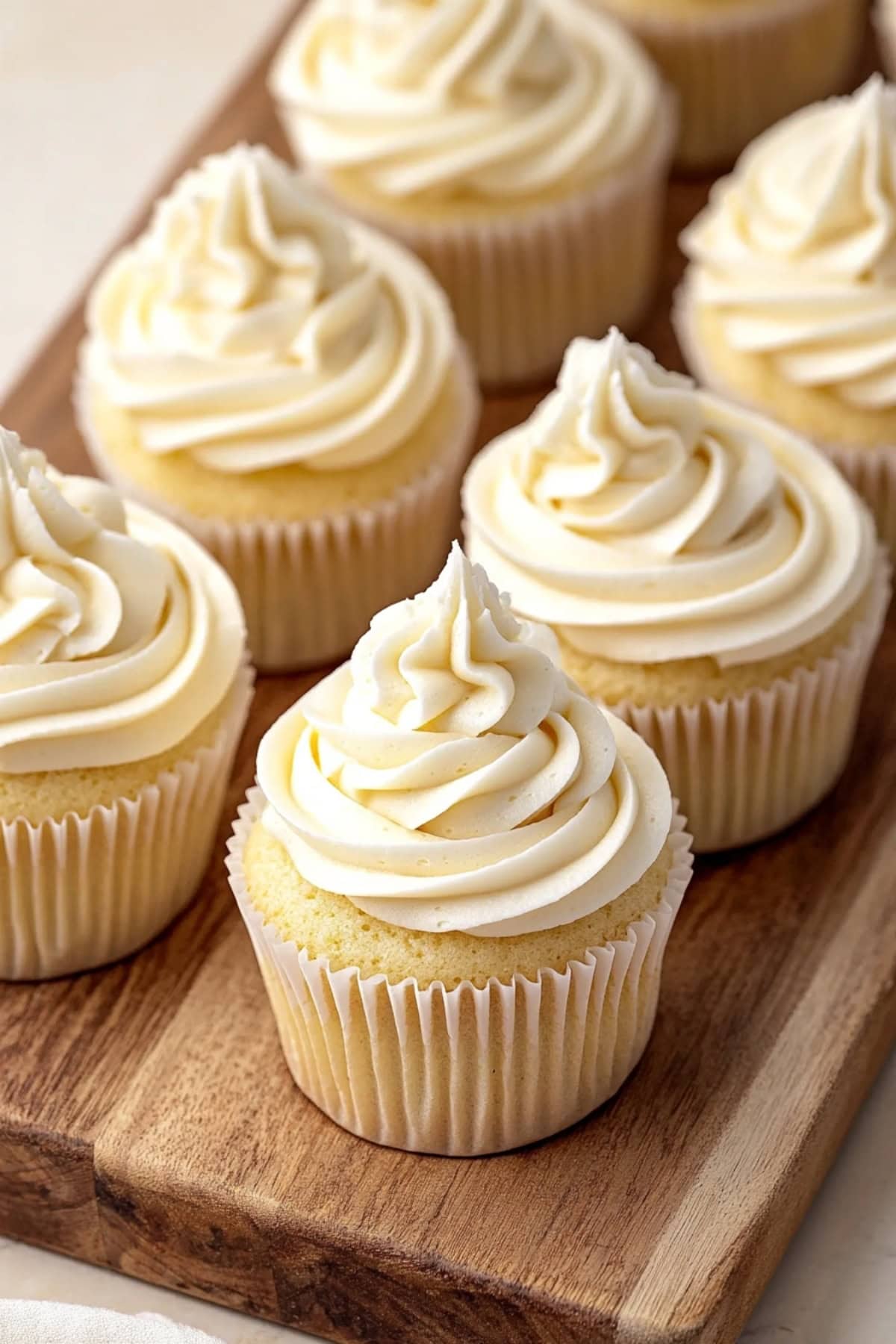 Close-up of white chocolate cupcakes with frosting on a wooden board.