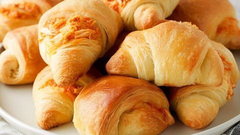 Crescent rolls filled with shredded buffalo chicken inside arranged in a white plate.