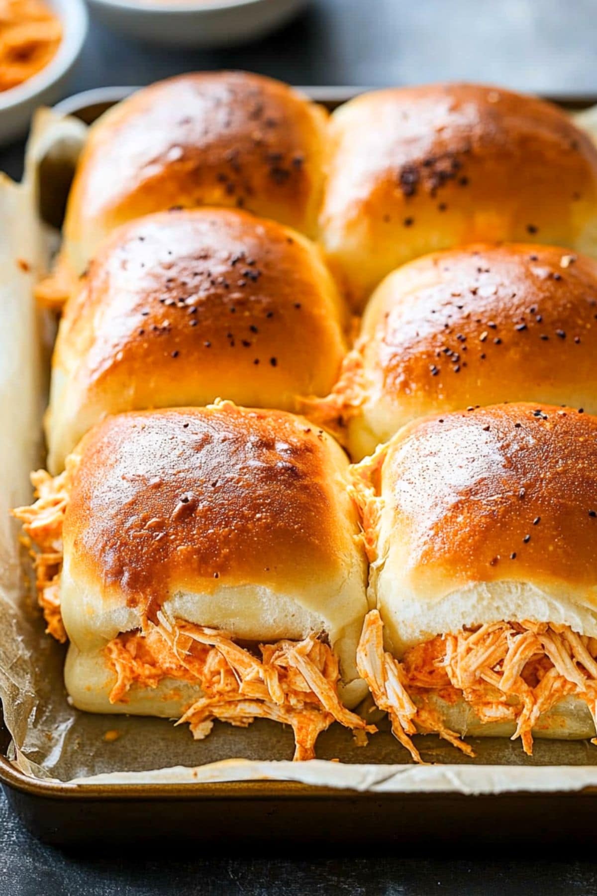 Hawaiian roll buns with shredded chicken buffalo sitting on a sheet pan with parchment paper.