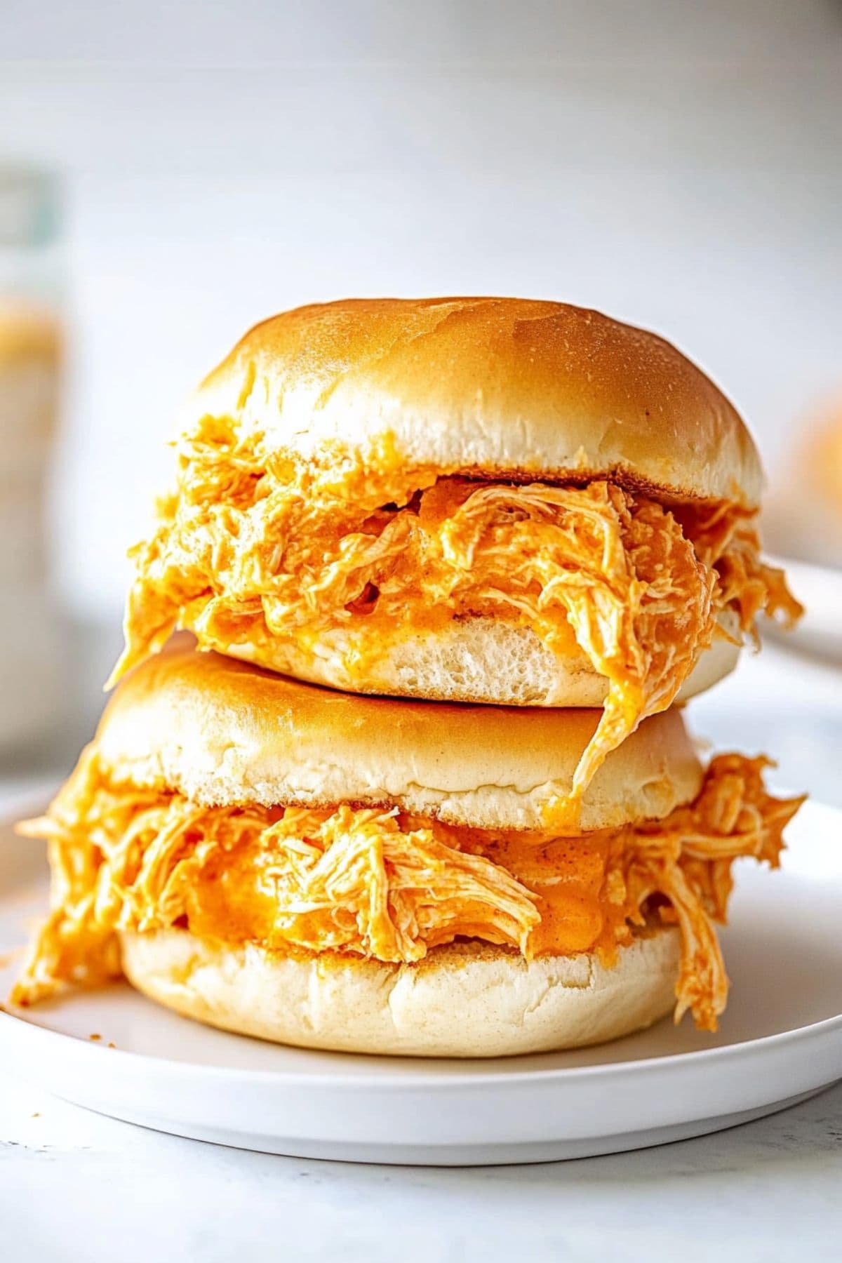 Two buns on top of each other with shredded chicken buffalo filling.