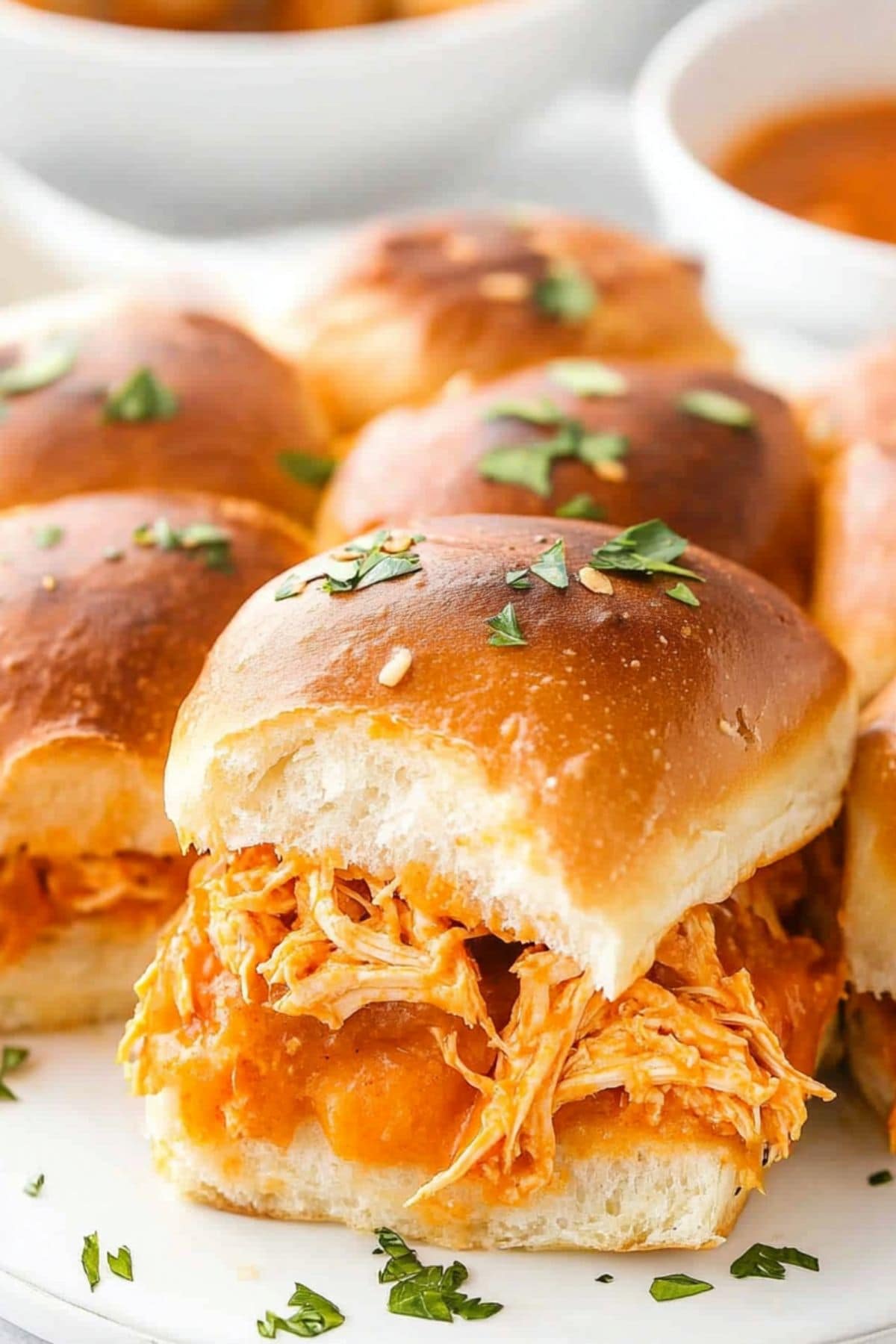 Hawaiian roll buns with shredded buffalo flavored chicken served in a white plate.