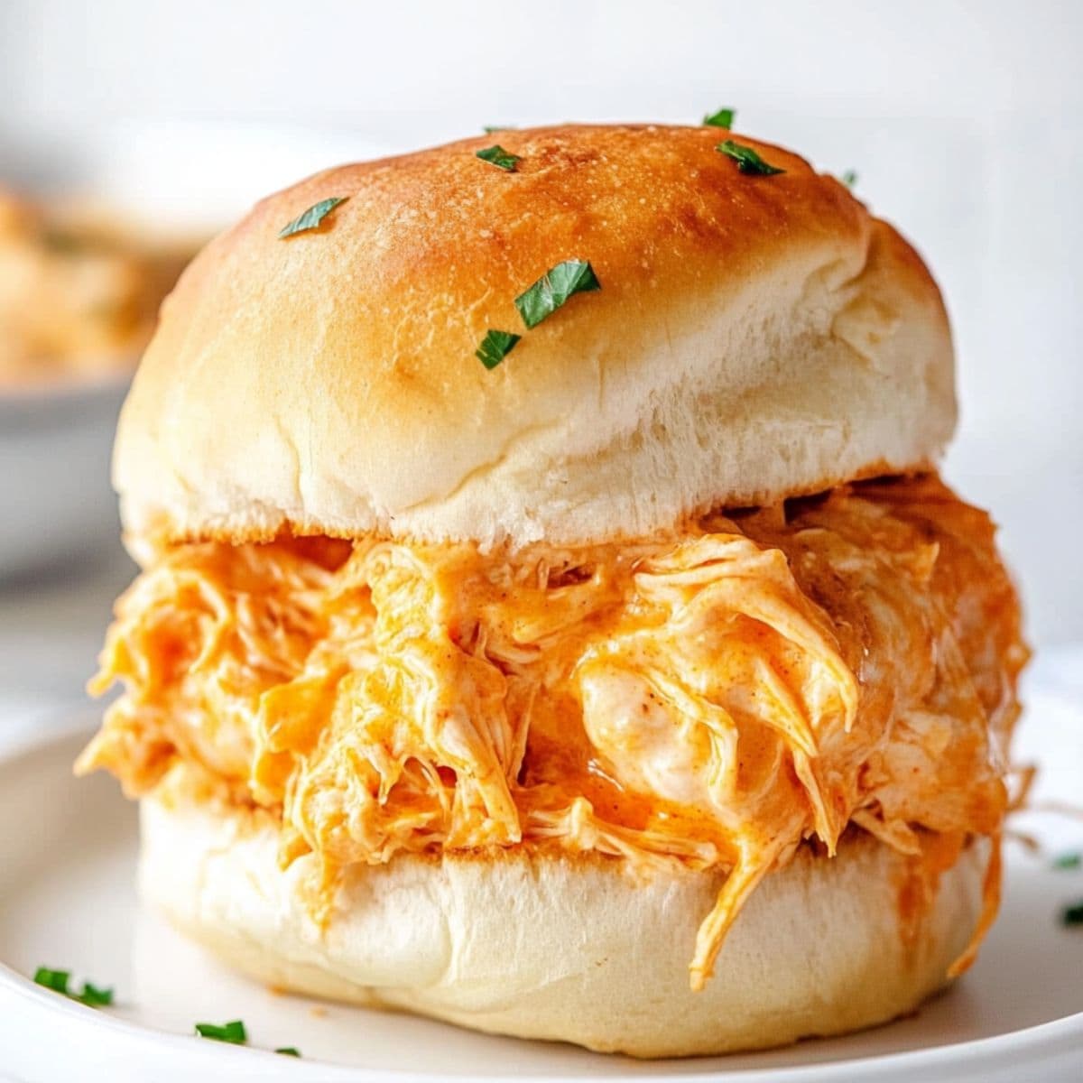 Bun with shredded buffalo chicken filling served in a white plate.