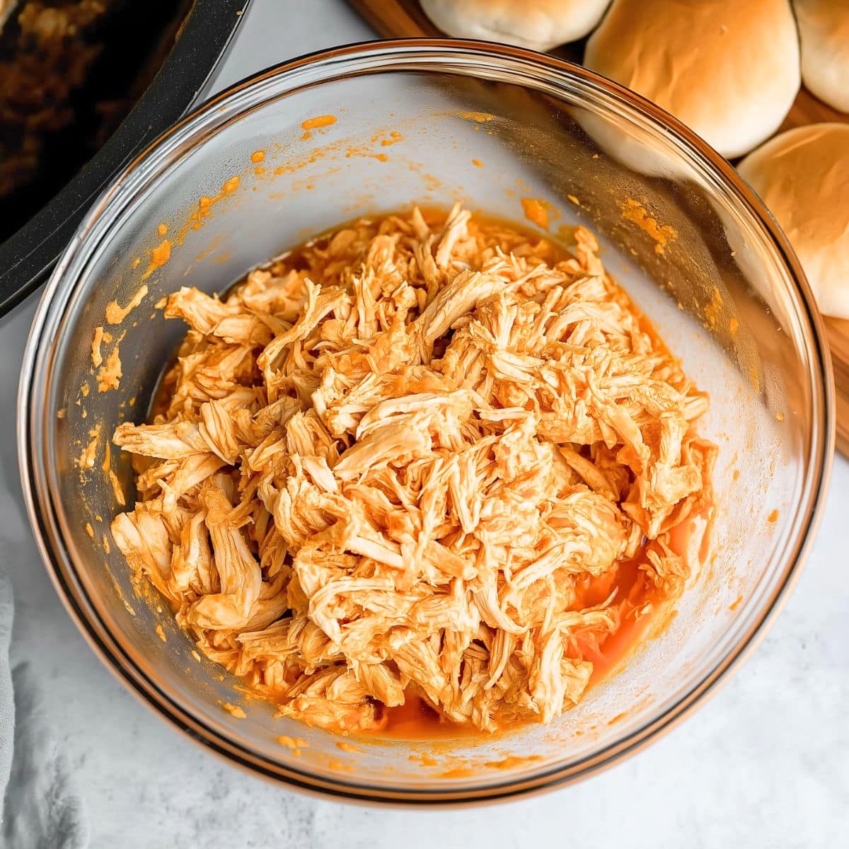 Shredded chicken with buffalo sauce in a glass mixing  bowl.