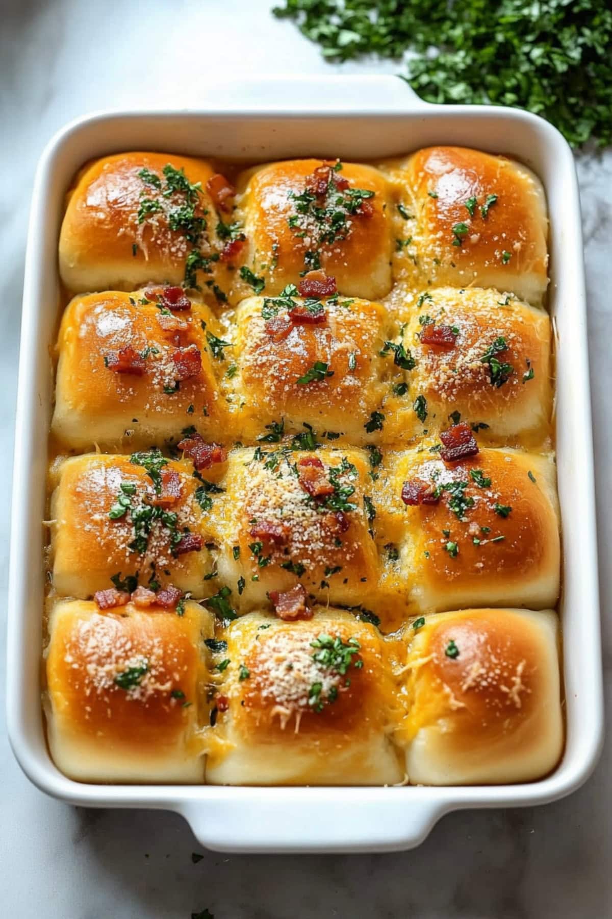 A baking dish filled with bacon ranch sliders with grated parmesan and chopped parsley.