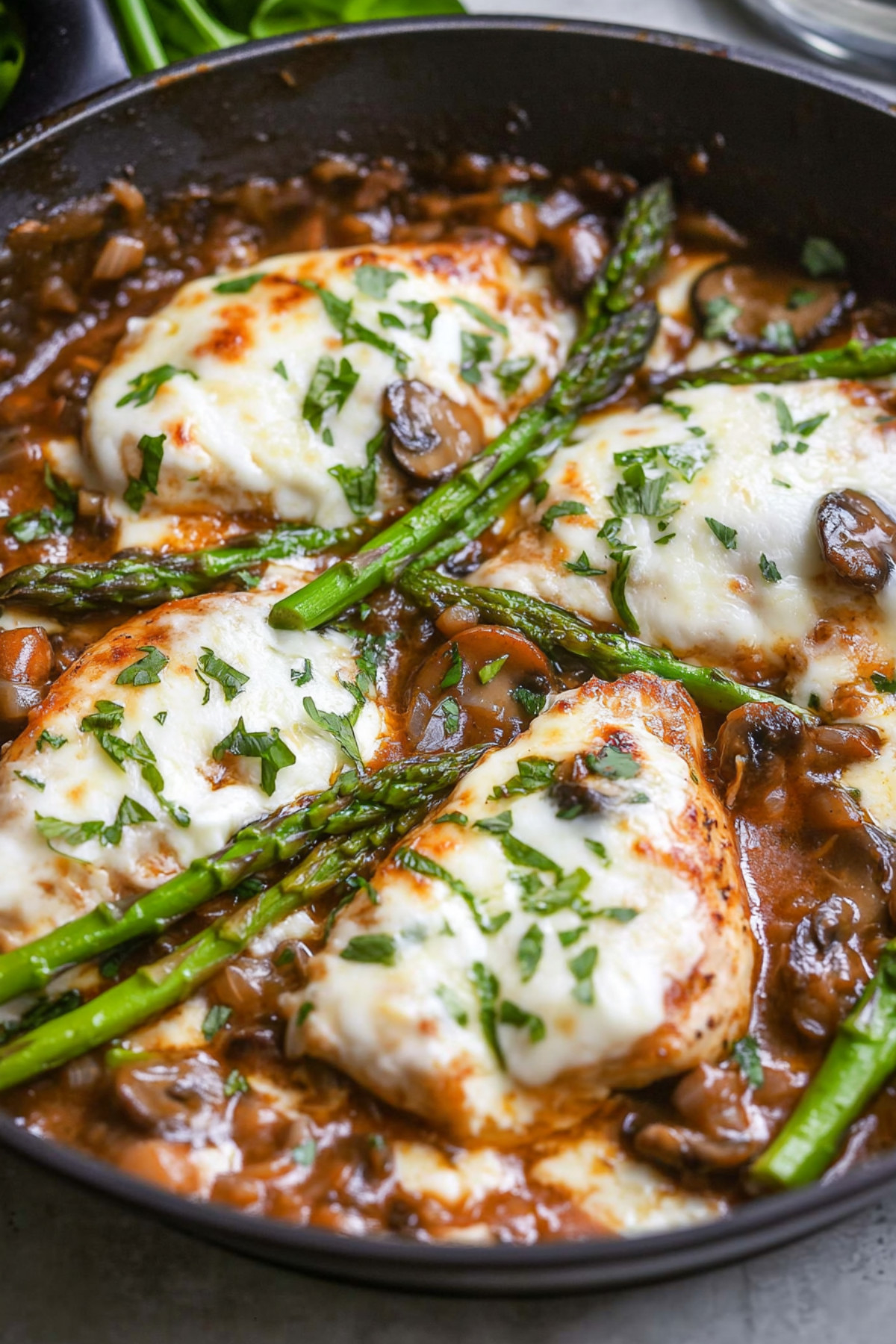 Chicken cutlets cooked in creamy mushroom sauce topped with melted cheese and asparagus in a skillet pan.