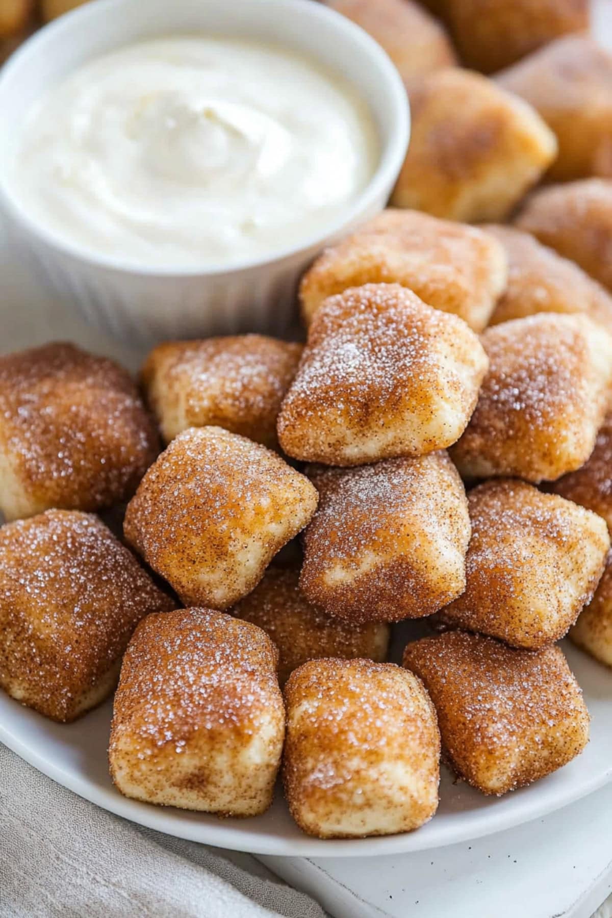 Bunch of cinnamon sugar pretzels bites in a white plate served with cream cheese dip in a ramekin dish.