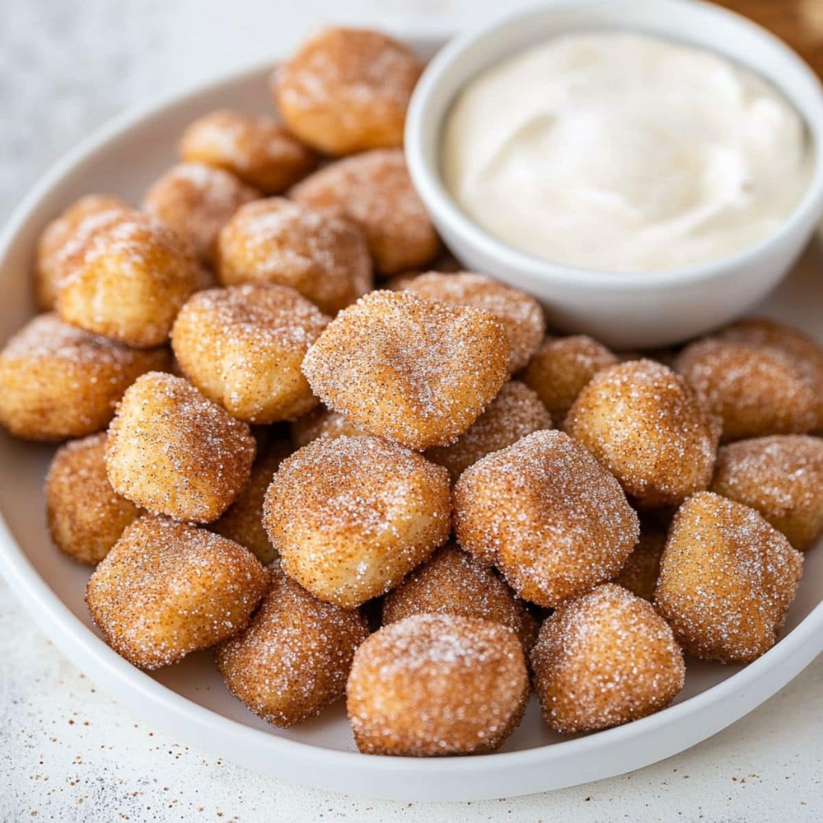 Soft cinnamon sugar pretzel bites served on a white plate with cream cheese dip in a ramekin.