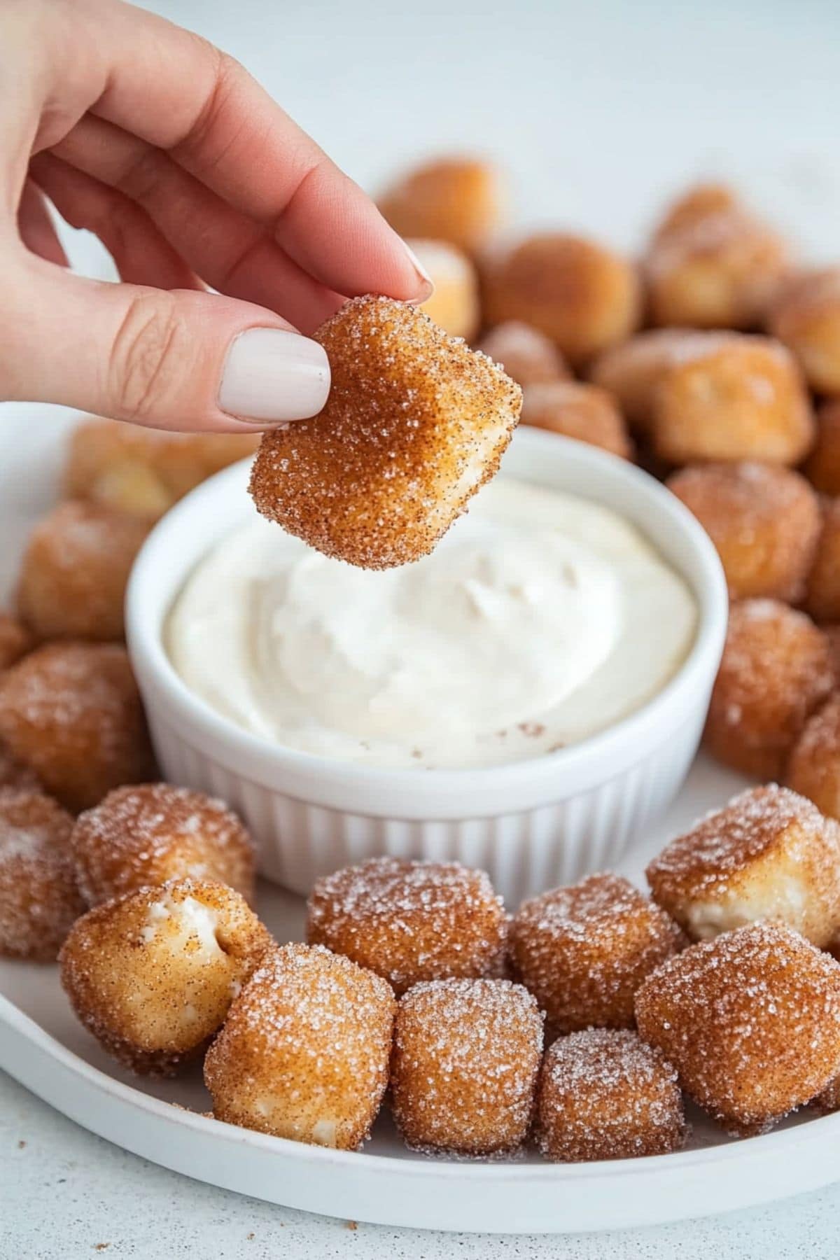 Hand holding a cinnamon sugar pretzel bite over a ramekin dish with cream cheese dip.