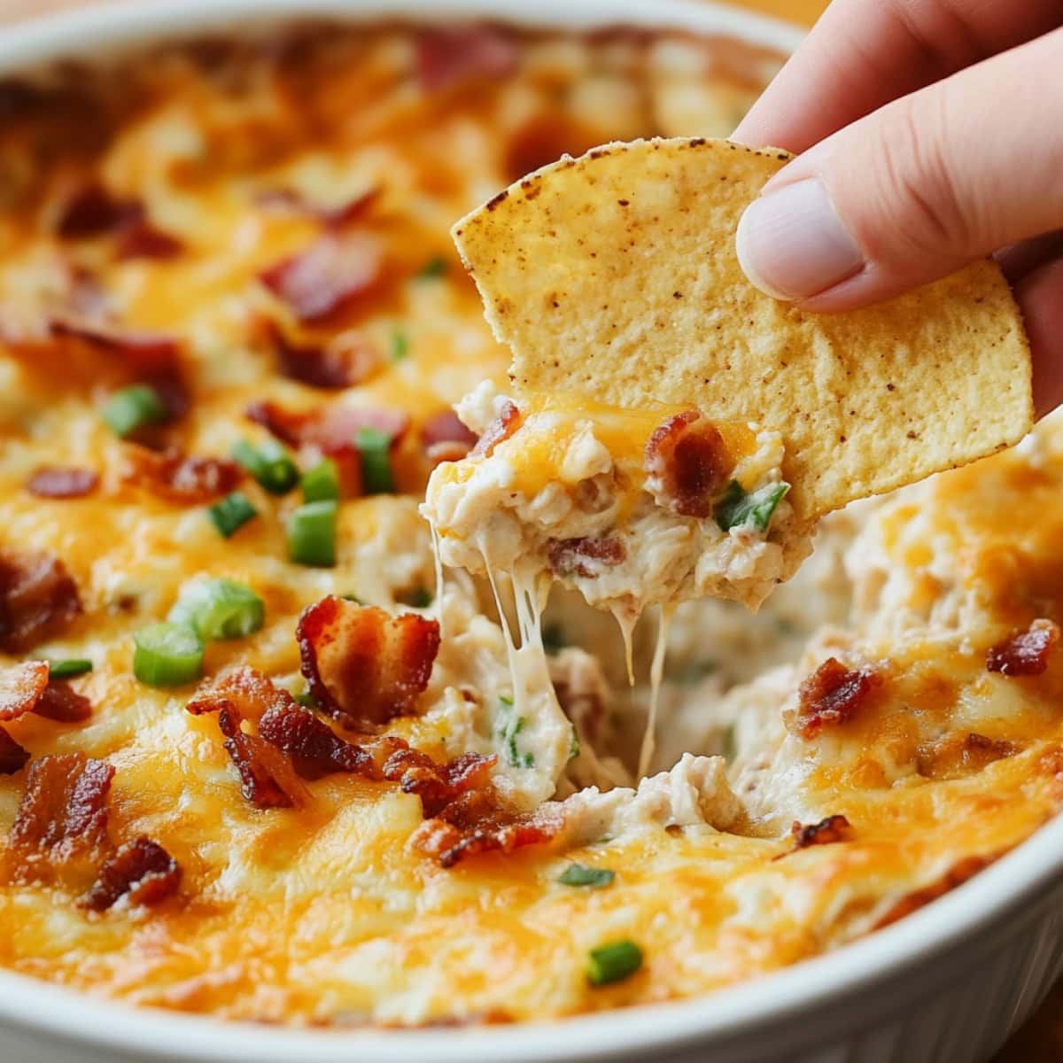 A hand dipping a chip into a bowl of cheesy crack chicken dip.