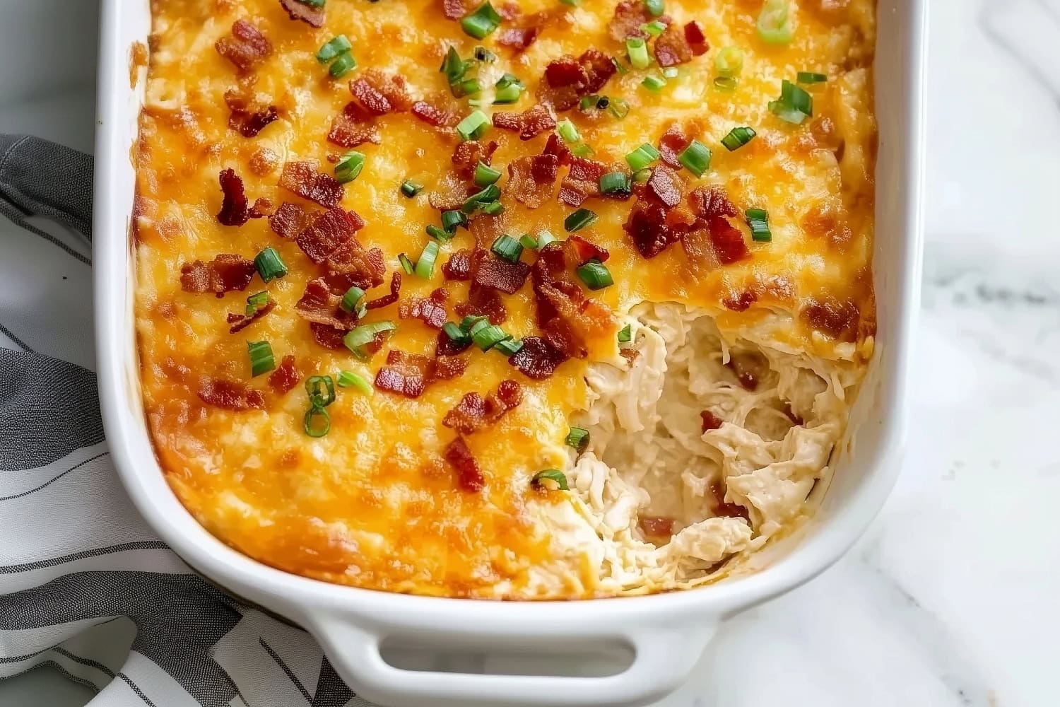 A creamy crack chicken dip in a baking dish, with melting cheese on top, and sprinkled with bacon bits and green onions.