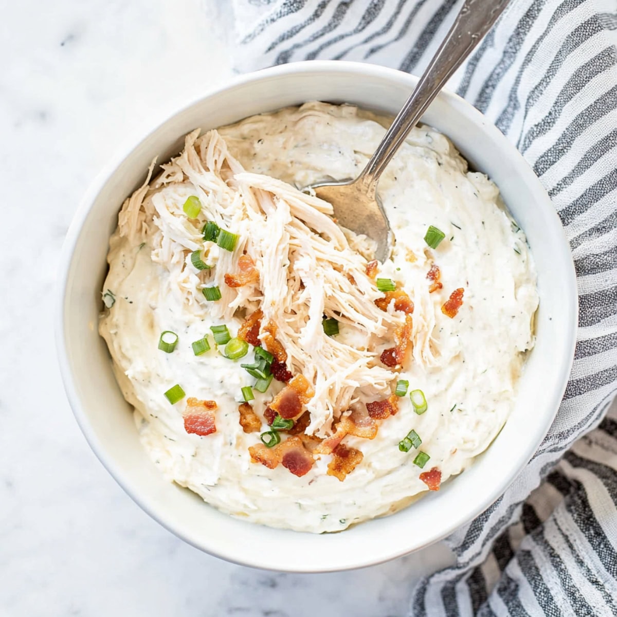 Cream cheese with shredded chicken, bacon bits and chopped green onions in a bowl.