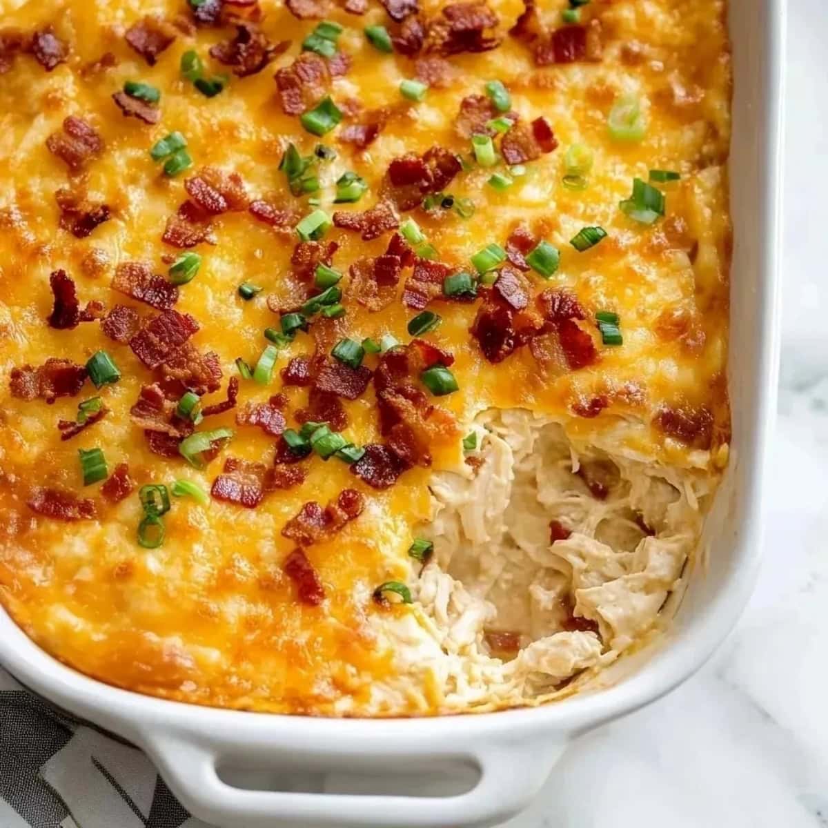 A baking dish filled with cheesy crack chicken dip with bacon and chopped green onions.