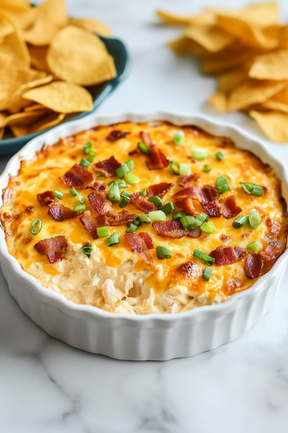 Homemade cheesy crack chicken dip with bacon and chopped green onions, served with chips on the side.