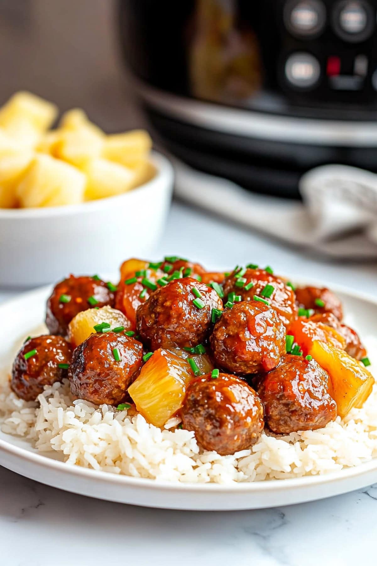 Crockpot Hawaiian meatballs with pineapple chunks, garnished with green onions and served with rice.