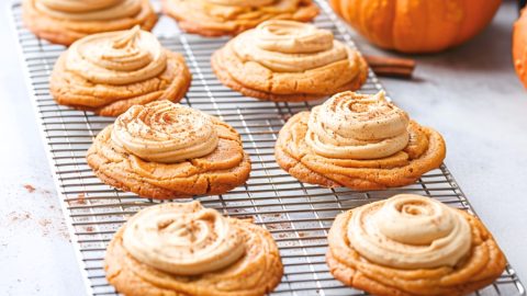 Cream frosting covered pumpkin cookies sitting on a cooling rack.