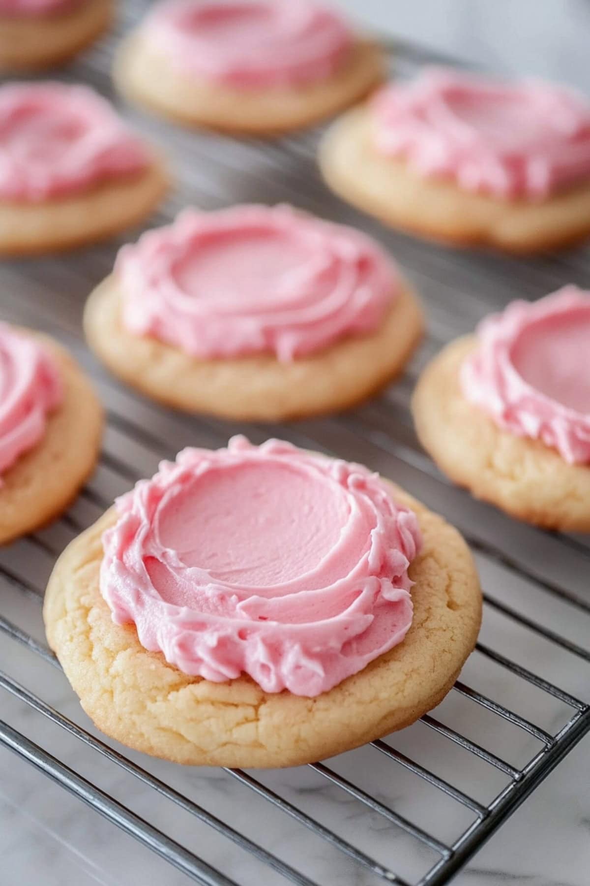 Crumbl sugar cookies topped with sweet frosting on a cooling rack.