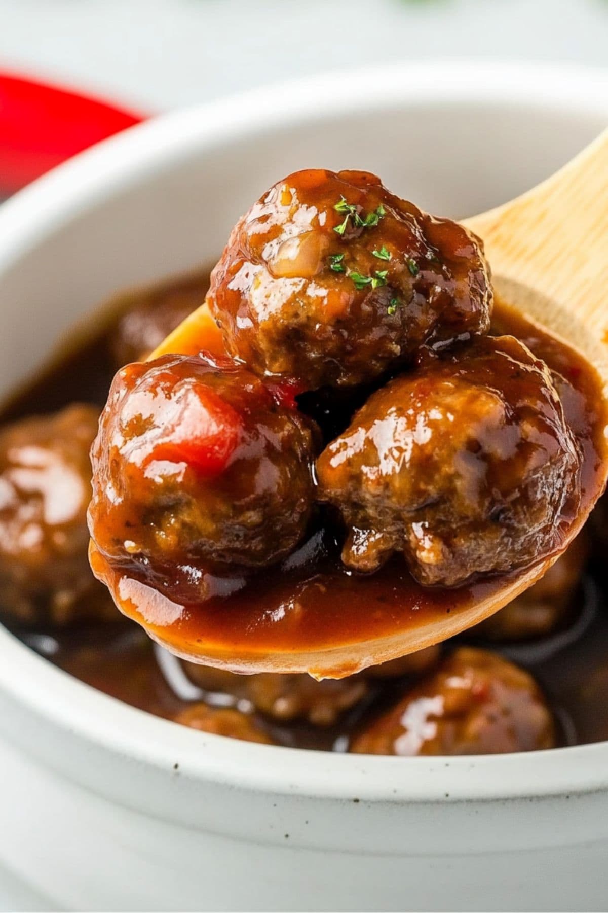 Wooden spoon with a scoop serving of meatballs soaked in a savory sauce served in a white bowl.