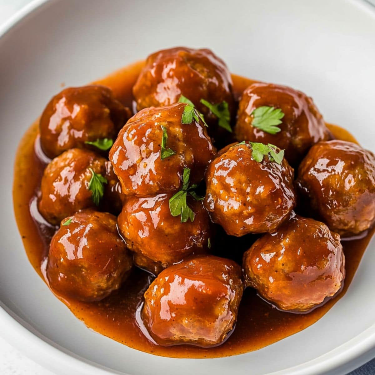 Meatballs cooked in savory sauce served in a white bowl.