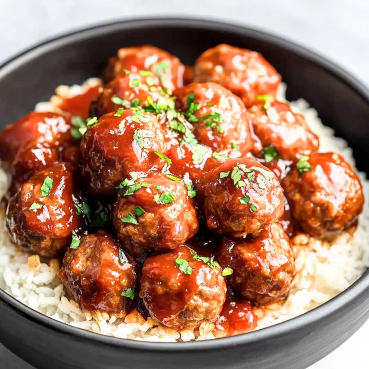 Meatballs served on top of white rice in a black bowl.