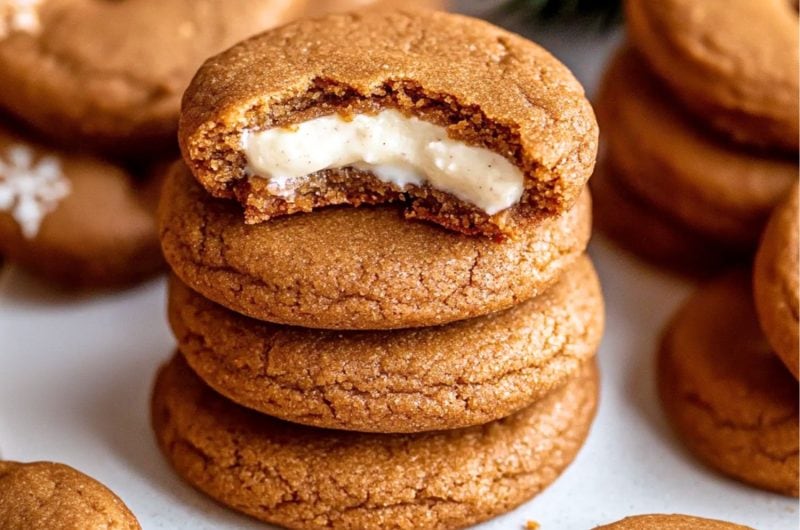 Gingerbread cookies filled with cheesecake stacked on top of each sitting on a white surface.