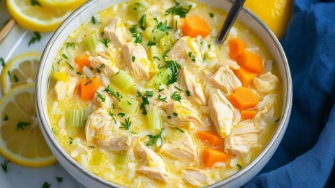 Greek lemon chicken soup served in a white bowl with scattered lemon slices on the side.