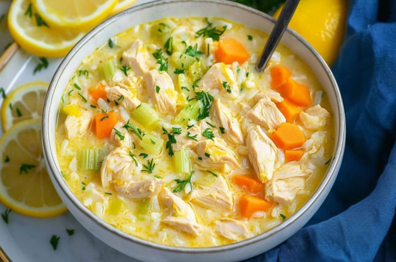 Greek lemon chicken soup served in a white bowl with scattered lemon slices on the side.