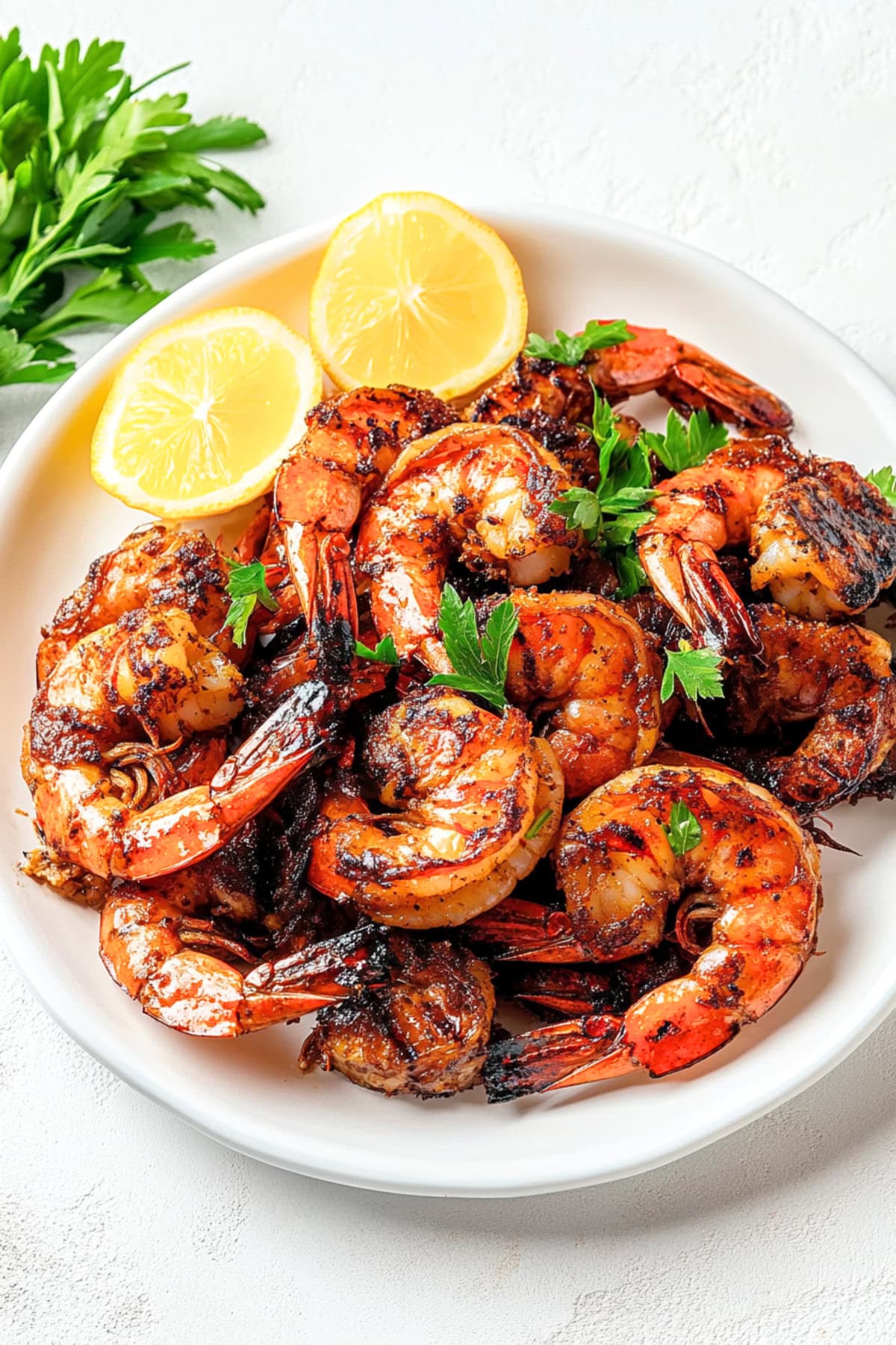 Grilled shrimp served on a white plate with fresh lemon and parsley.