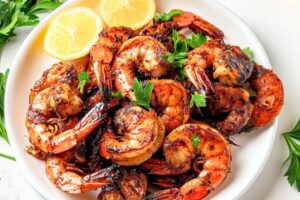 Grilled shrimps served in a white plate garnished with lemon wheel and chopped parsley.