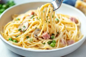 Serving of creamy ham tetrazzini in a white plate fork lifting pasta.