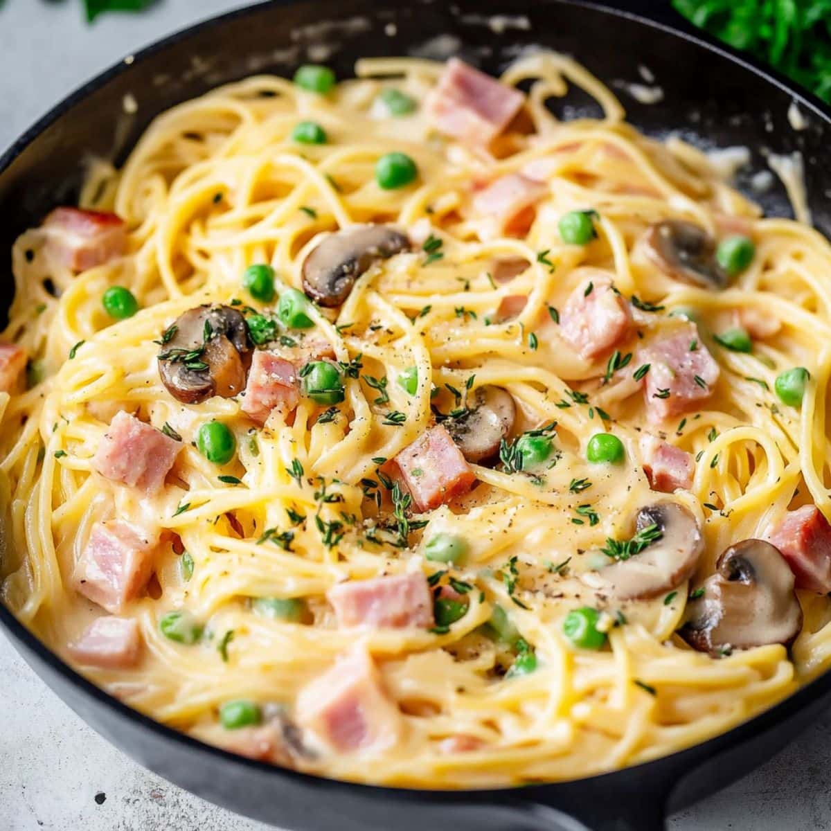 Spaghetti, ham, mushrooms, and peas with creamy and cheesy sauce tossed in skillet pan.