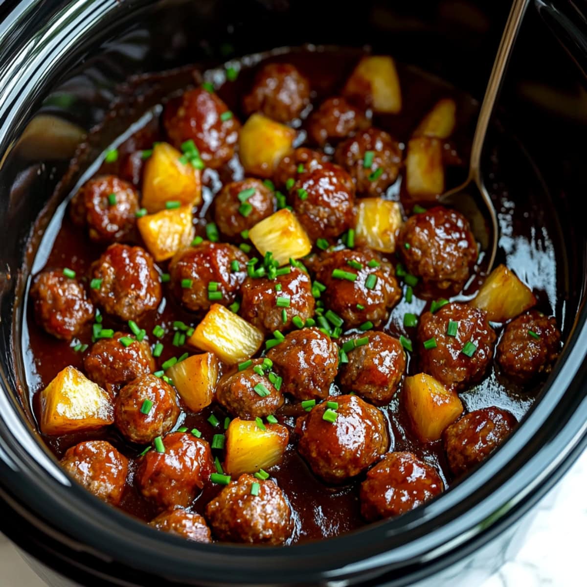 Saucy crockpot Hawaiian meatballs, garnished with chopped chives.