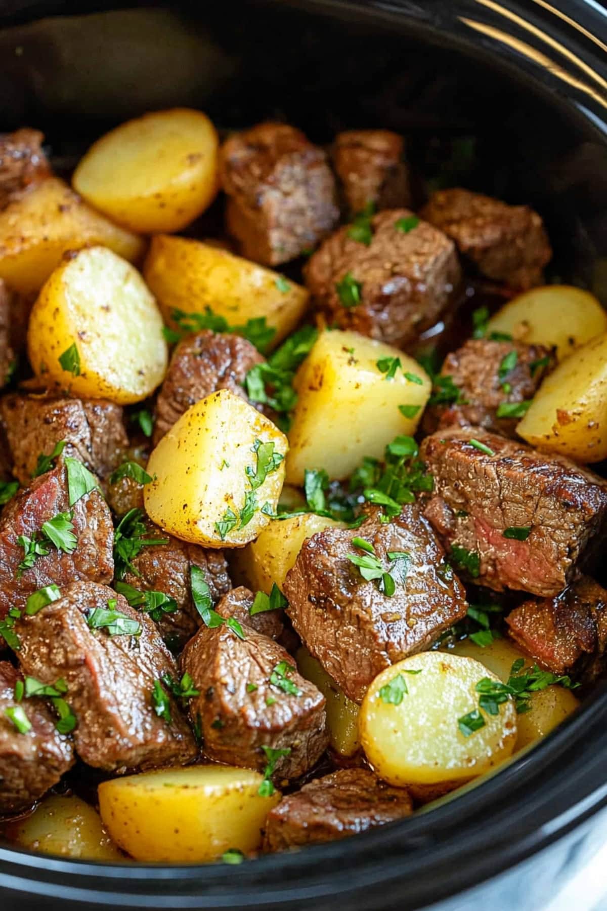 Cubed steak and golden potatoes in a slow cooker, close up