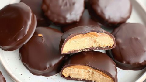 Bunch of chocolate coated shortcake cookies with a spread of peanut butter inside served in a white plate.