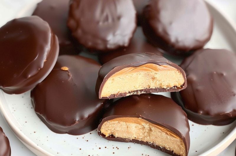 Bunch of chocolate coated shortcake cookies with a spread of peanut butter inside served in a white plate.