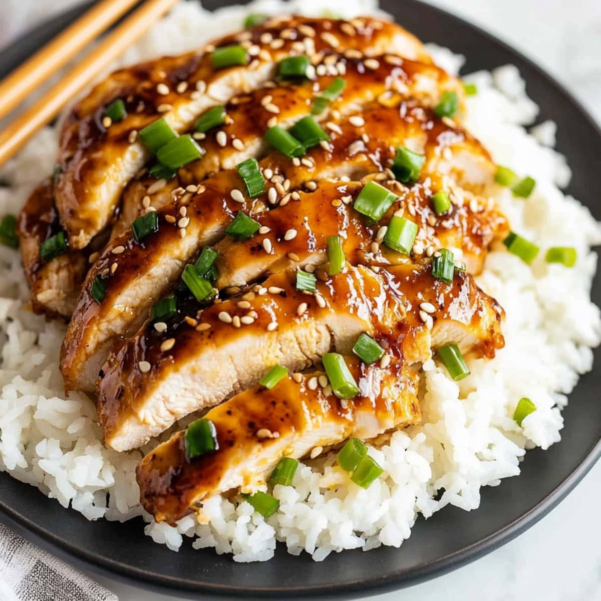 Sliced honey garlic chicken with sesame seeds and green onions, served with steamed rice.