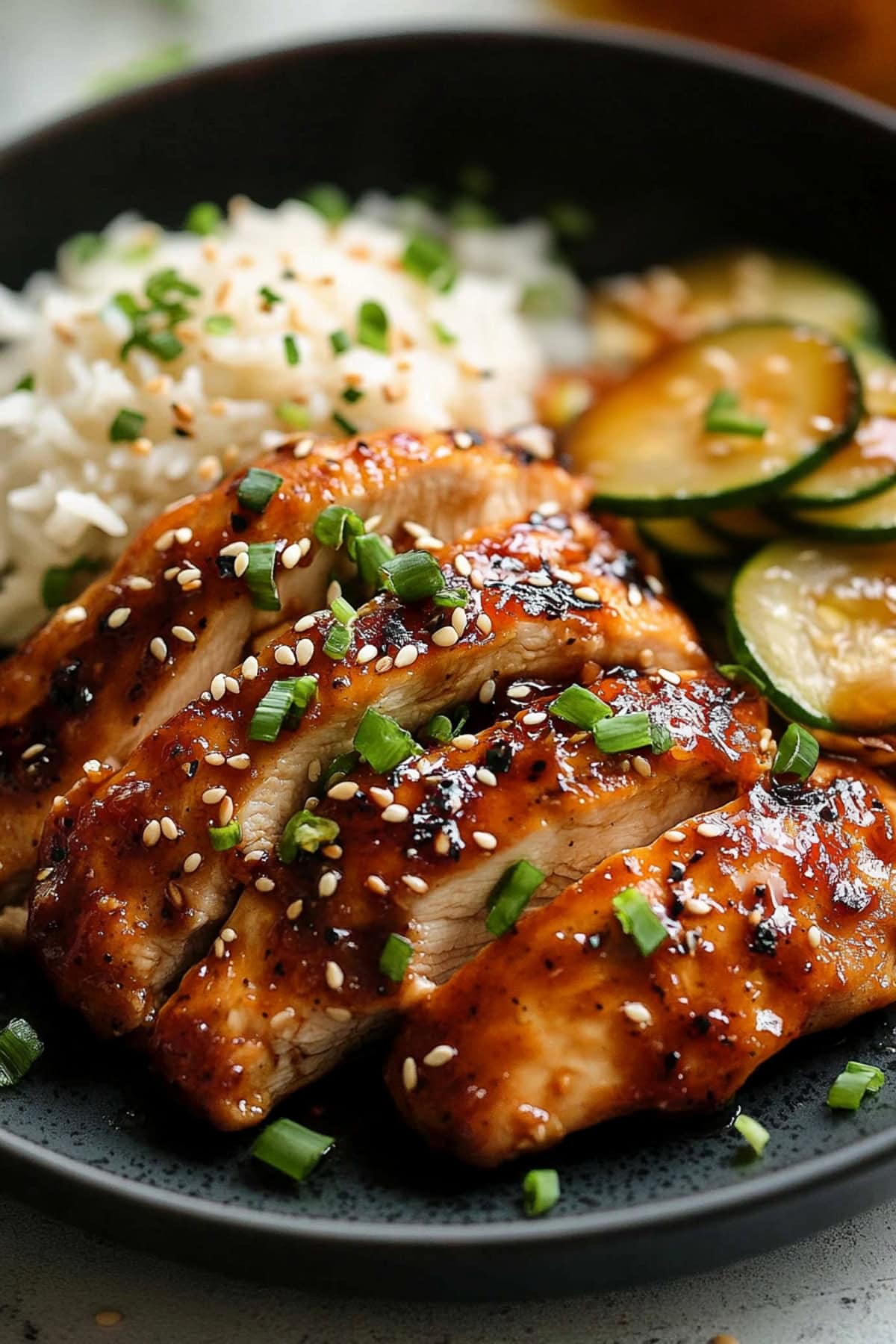 Close-up of honey garlic chicken with sesame seeds and green onions with rice and zucchini.