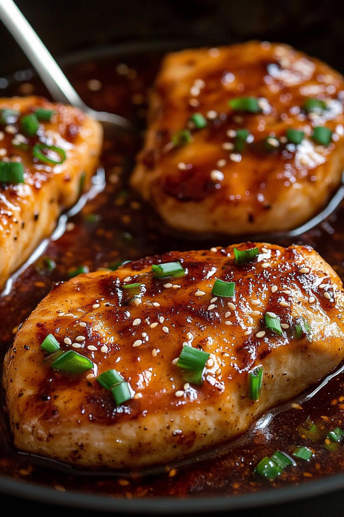 Close-up of a juicy honey garlic chicken thigh coated in a rich sauce in a skillet.