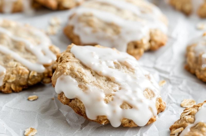 Oatmeal cookies with icing sitting on a white parchment paper.