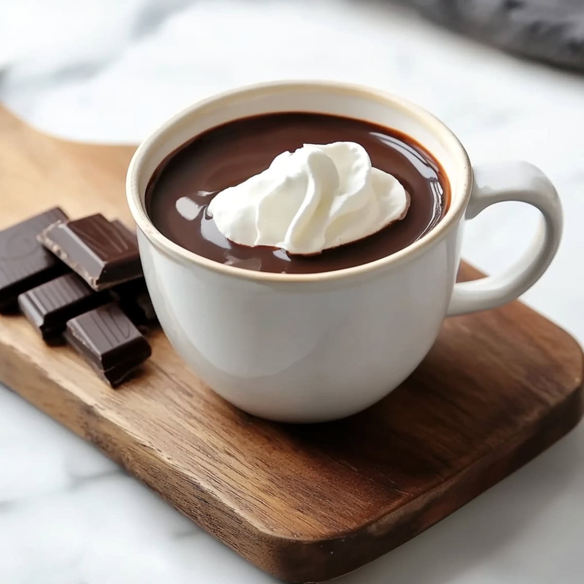 A cup of Italian hot chocolate topped with a dollop of whipped cream on a wooden board.