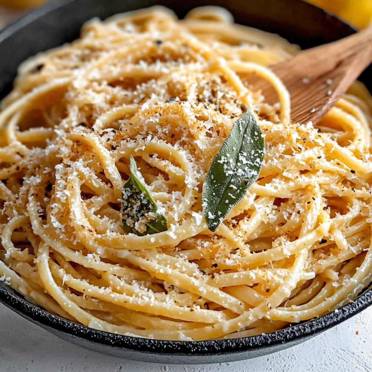 Linguine pasta tossed in butter sauce with sage leaves and grated cheese in a skillet pan.