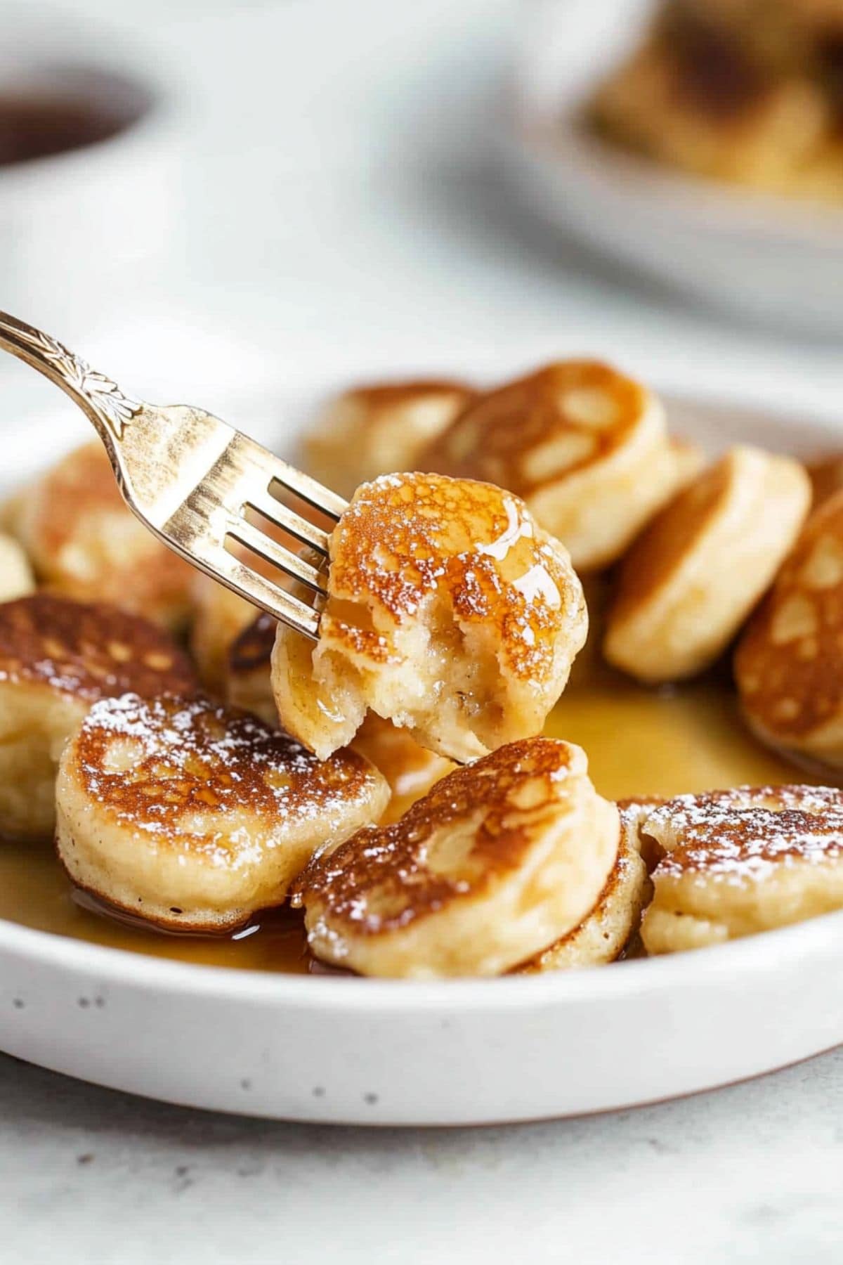 Mini banana pancake bite picked by a fork from a serving in a plate.