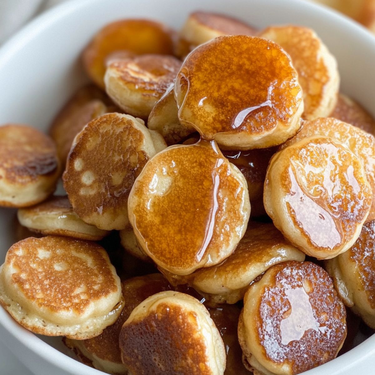 Bunch of pancake coated banana slices in a white bowl drizzled with maple syrup.