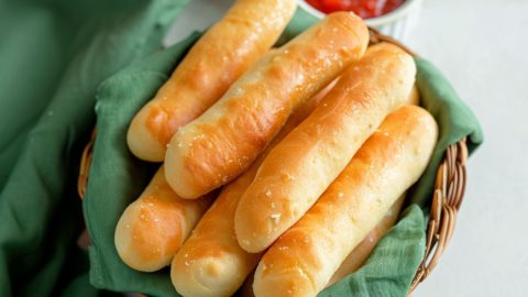 Golden, buttery breadsticks arranged in a basket lined with a green cloth.